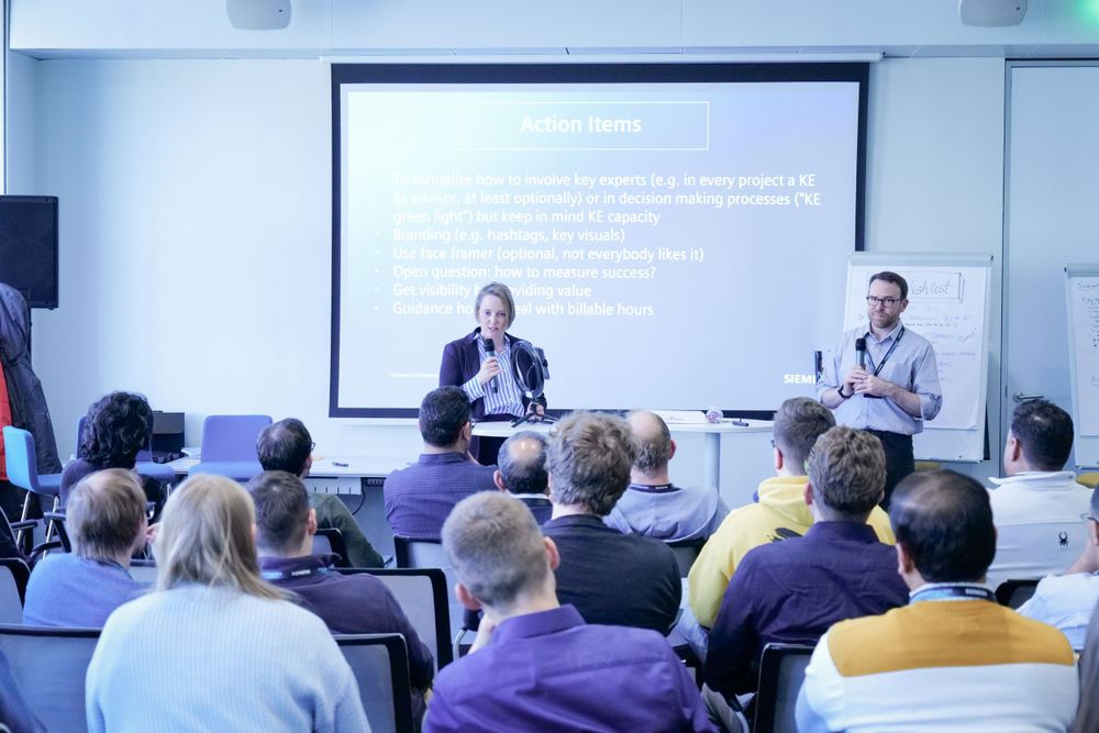 Two presenters addressing an audience during a corporate seminar with projection screen.