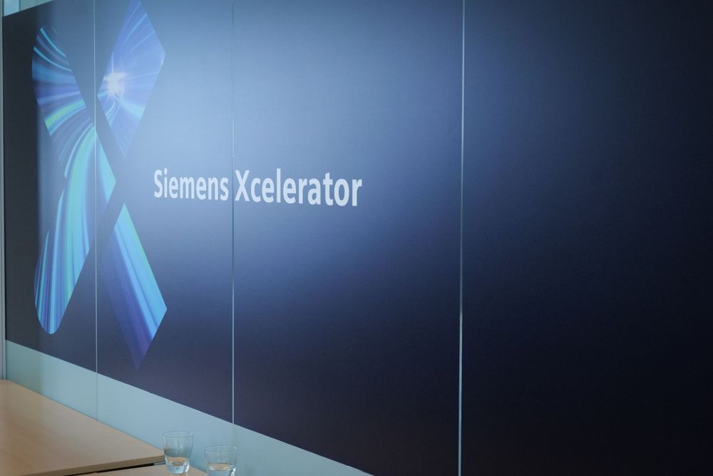Siemens Xcelerator branding displayed on a large dark blue screen at a corporate event.