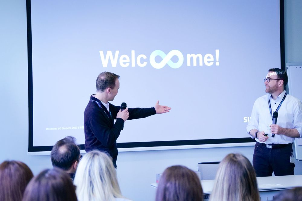 Speaker welcoming audience at a corporate event with Welcome sign on screen.
