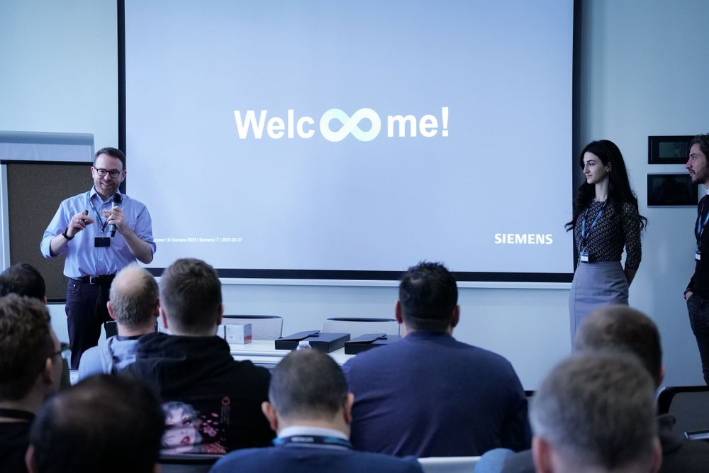 Siemens presenters welcome attendees with Welcome infinity sign displayed on projection screen.