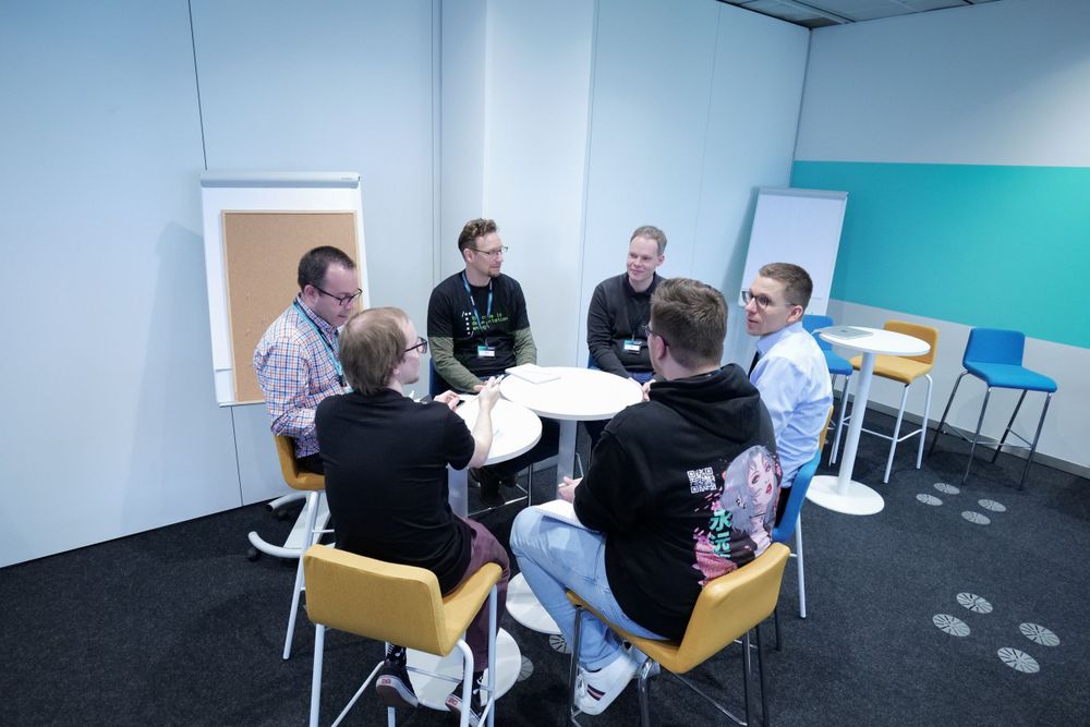 Six professionals engage in a collaborative roundtable discussion in a modern meeting space.