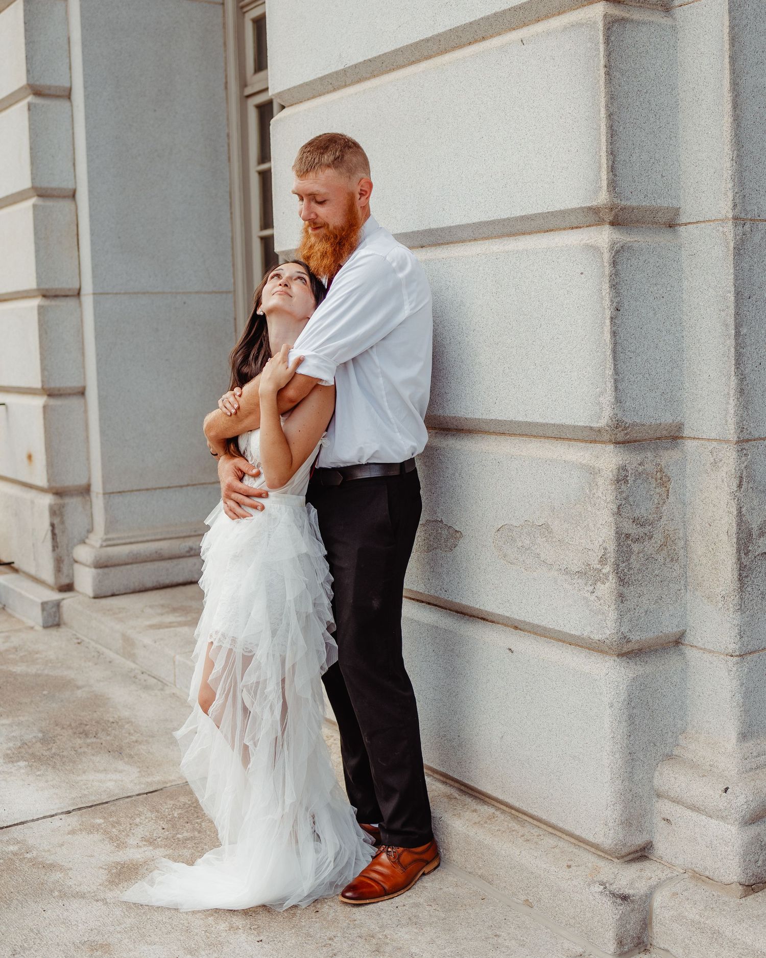 Intimate wedding moment against white stone building wall.