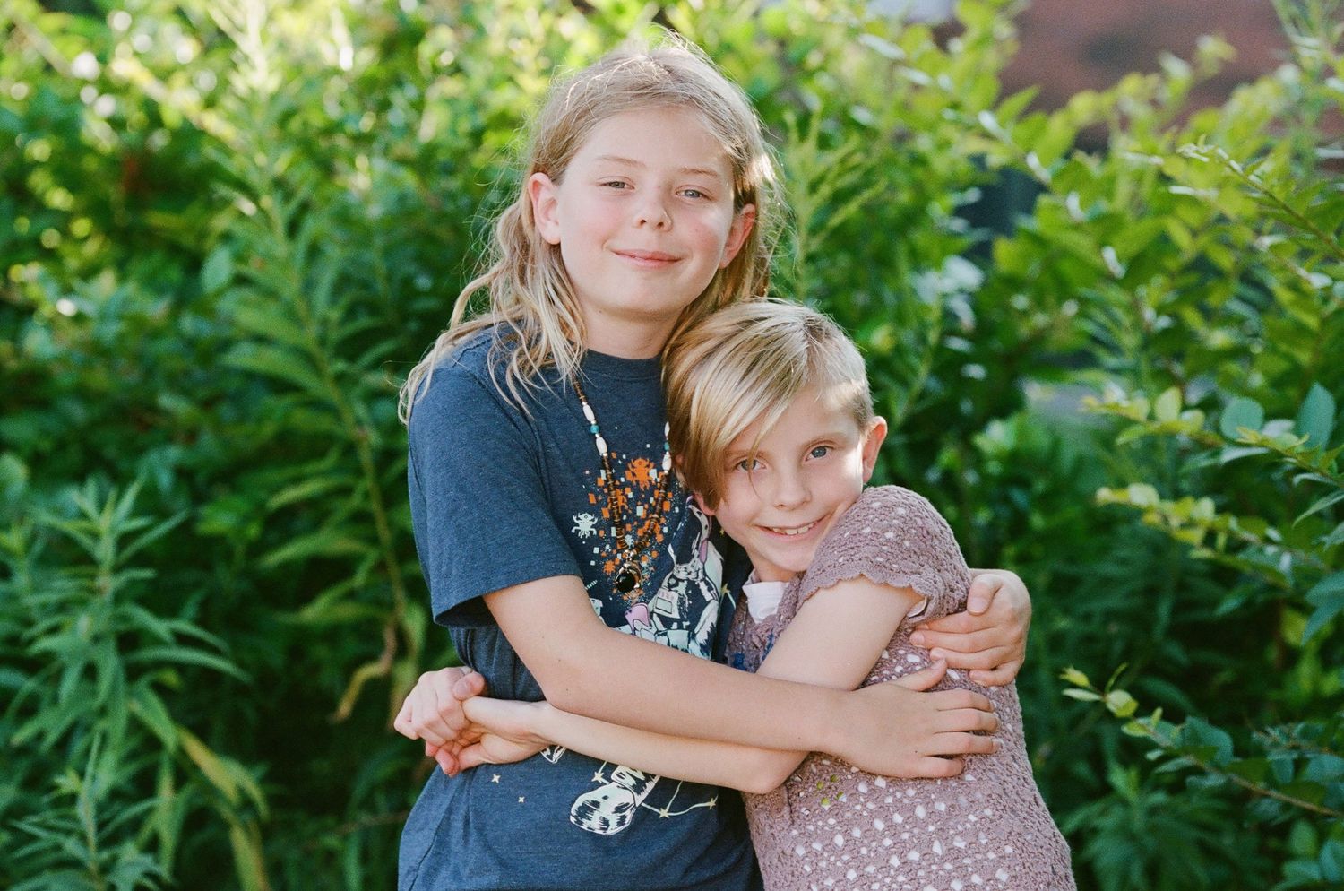 Two children hugging and smiling together in a sunny garden setting.