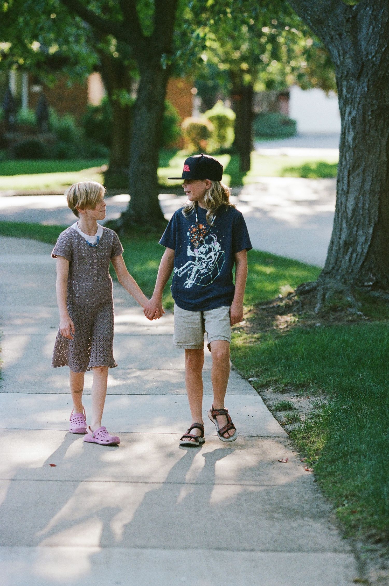 Two children walking together on a sidewalk on a sunny summer day.