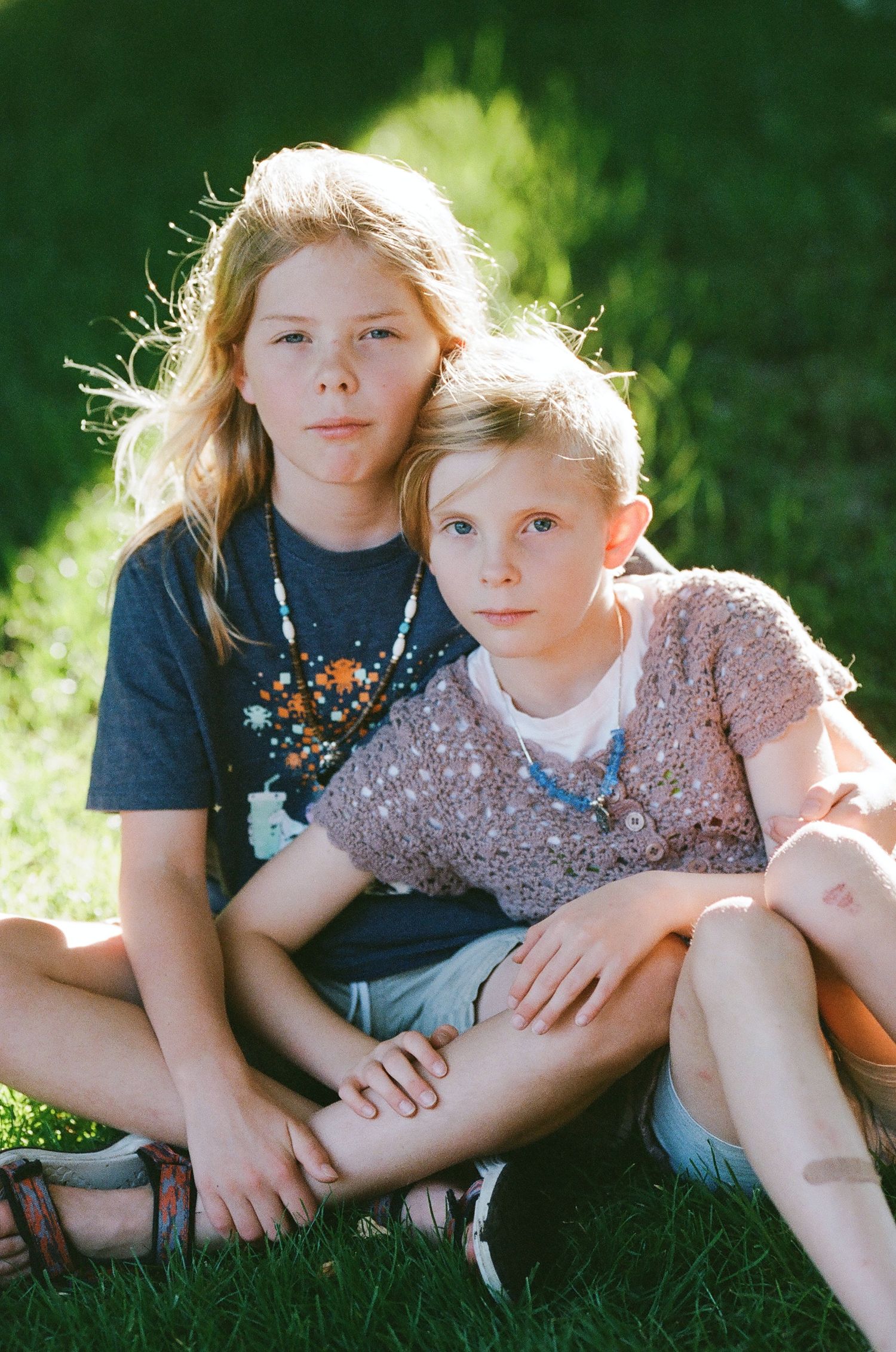 Two children sitting together on green grass in summer sunlight.