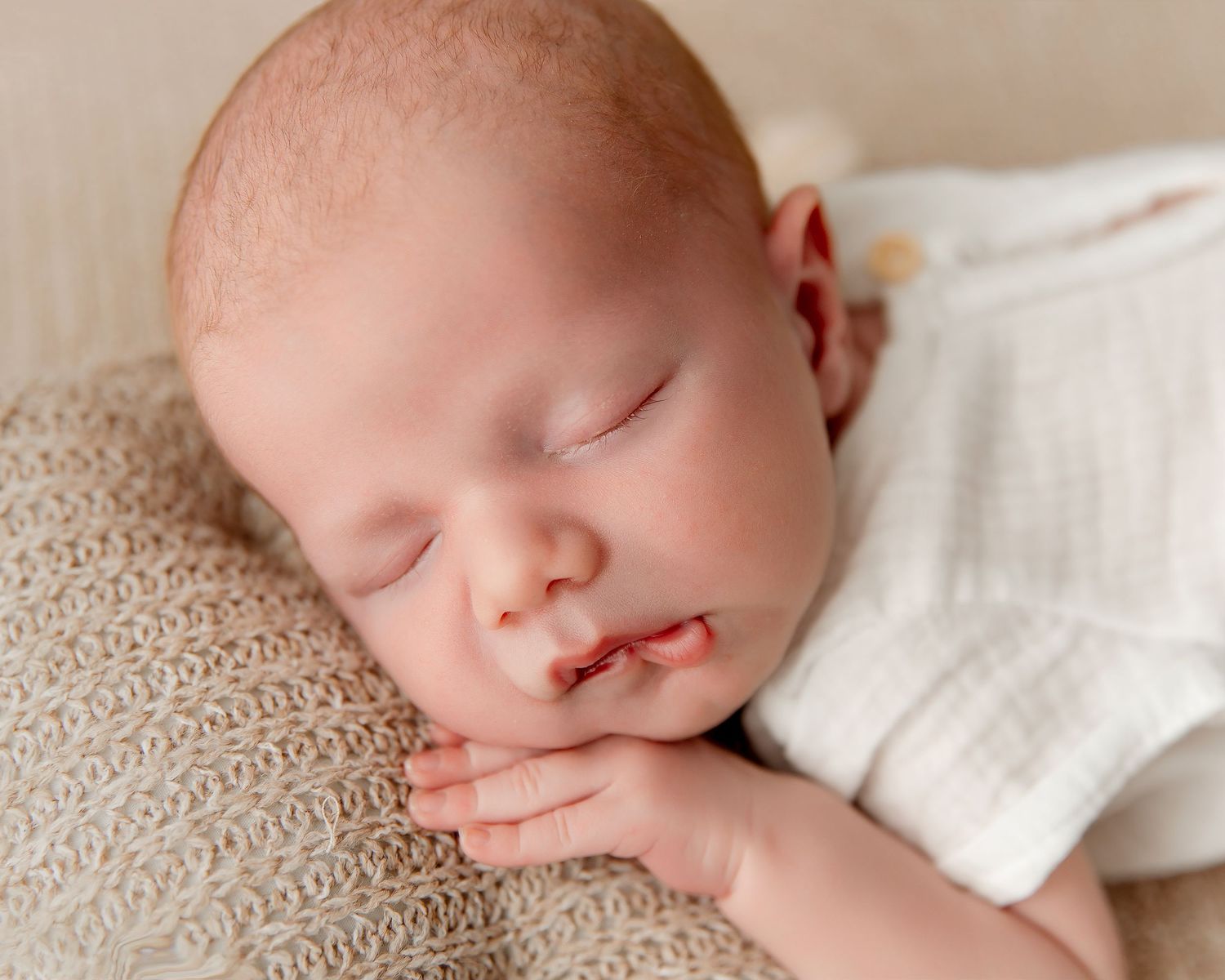 Sleeping infant in white dress resting in heart-shaped basket.