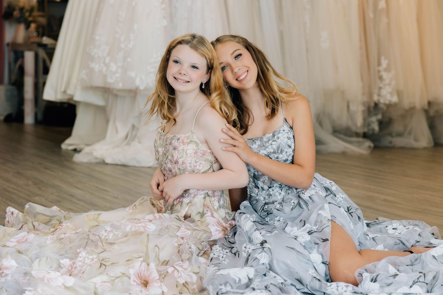 Woman and young girl posing together in floral dresses on floor of bridal boutique.