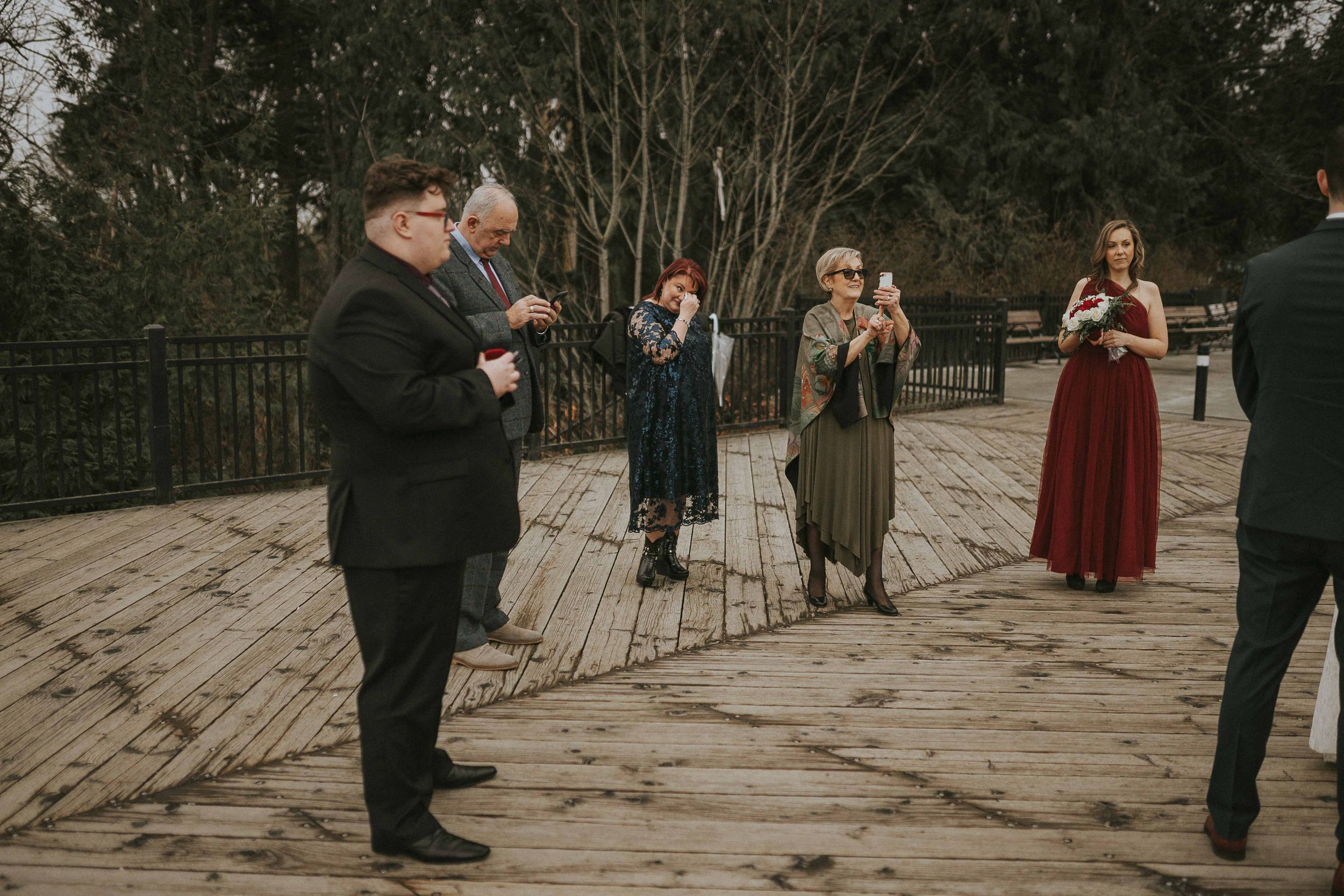 A group of people in vintage clothing gathering on a wooden deck in a moody outdoor setting.