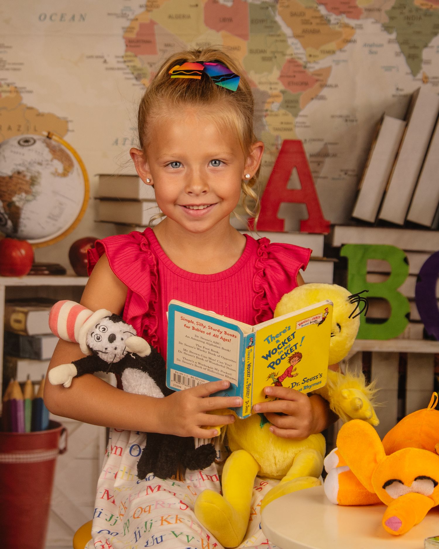 Educational photoshoot with stuffed animals, books, and world map background.
