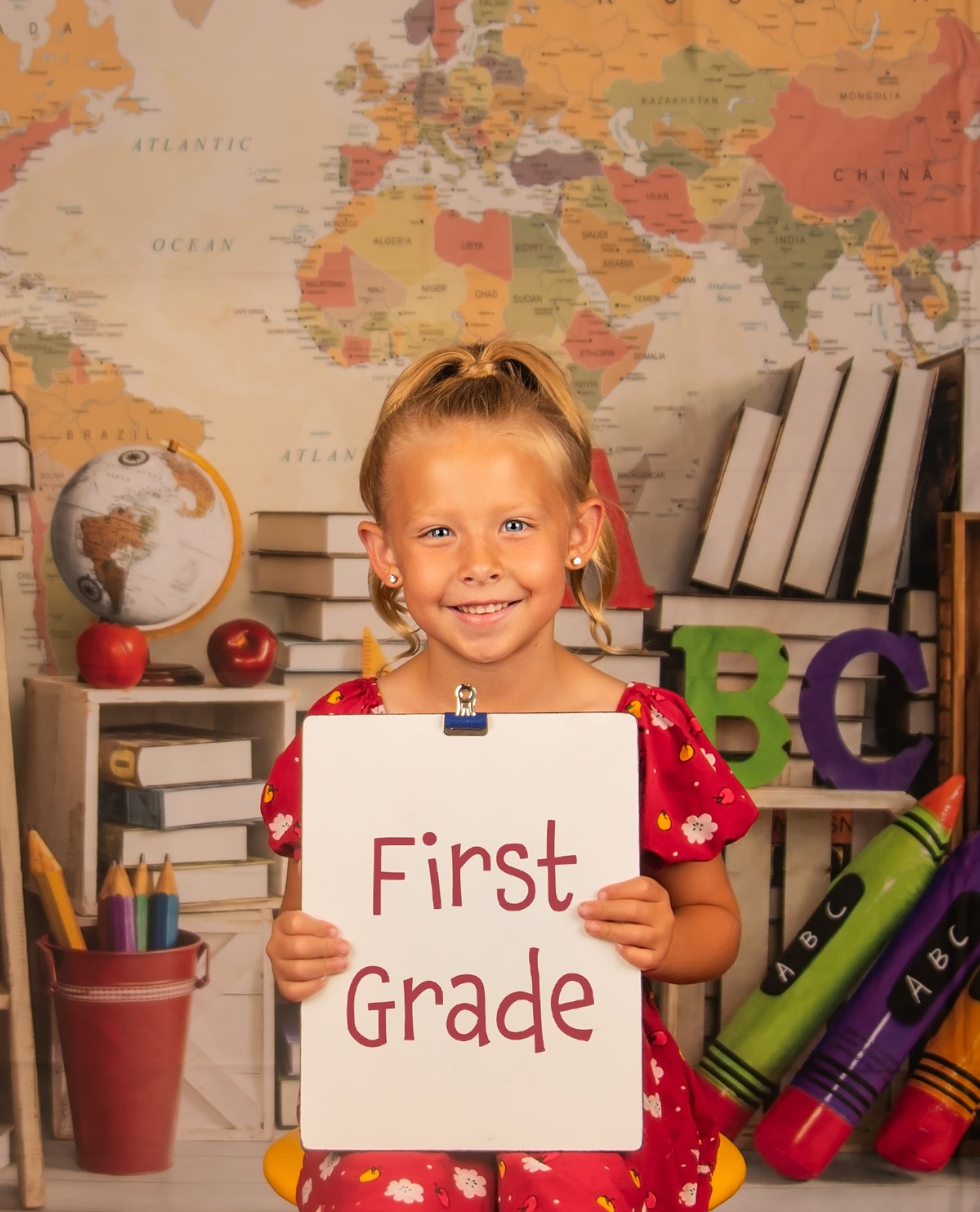 Back to school photo with first grade sign against world map and educational props.