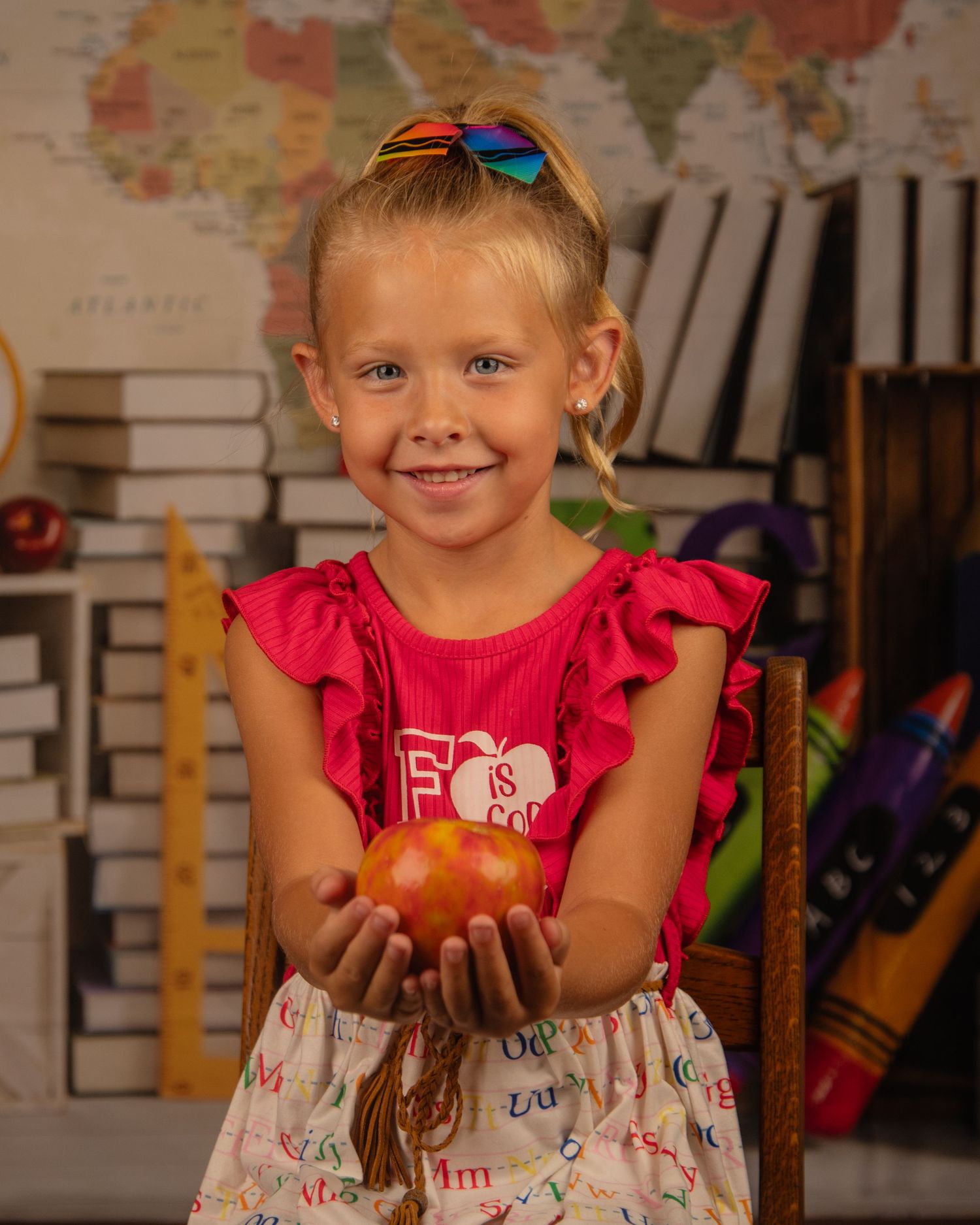 Student holds a red apple in front of world map backdrop with educational elements.
