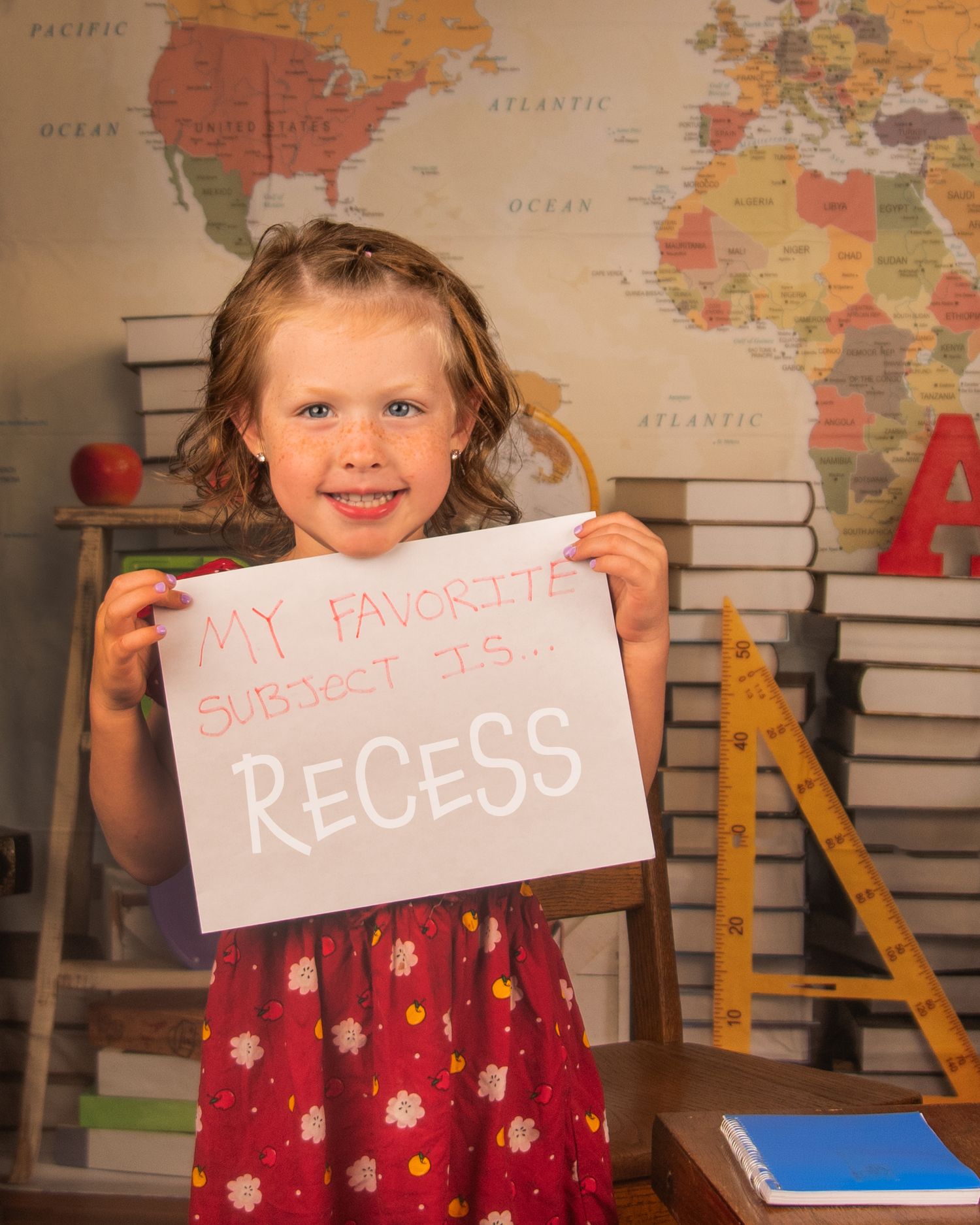 School-themed photo showing sign that reads 'recess' against world map background.