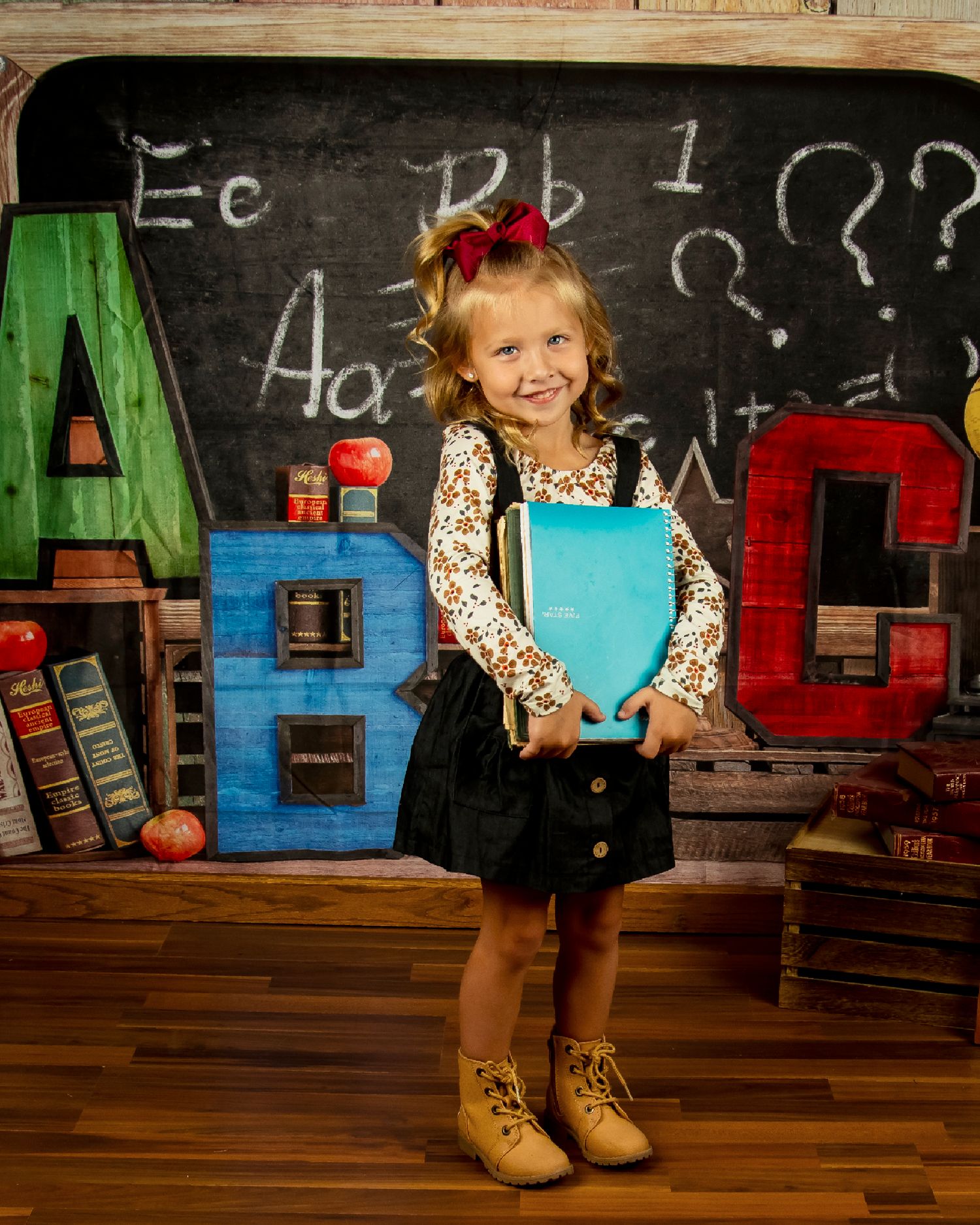 A classroom setting with colorful ABC letters, chalkboard background, and a young student holding a blue book.
