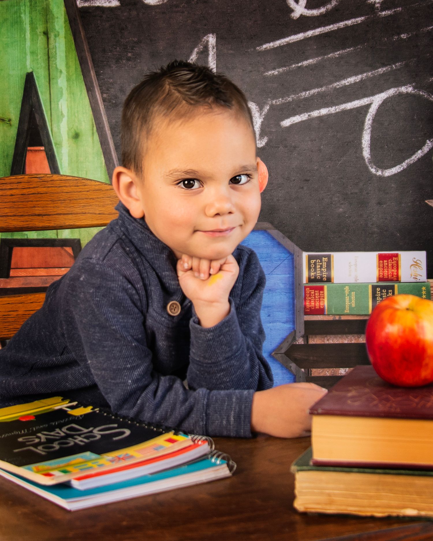Educational portrait with books and apple against chalkboard backdrop.