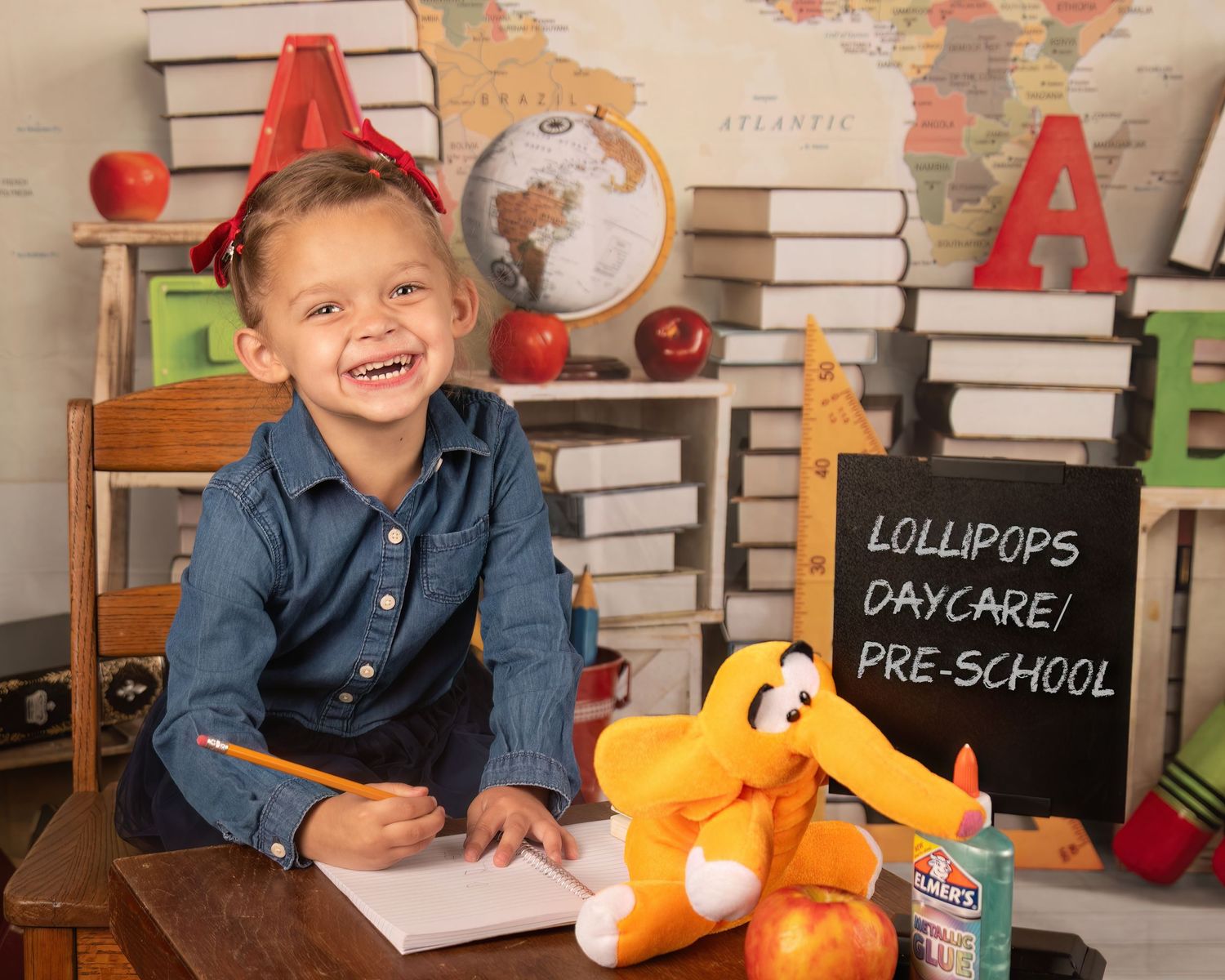 School setting with stacked books, colorful letters, and toys including a plush orange giraffe and red apples.