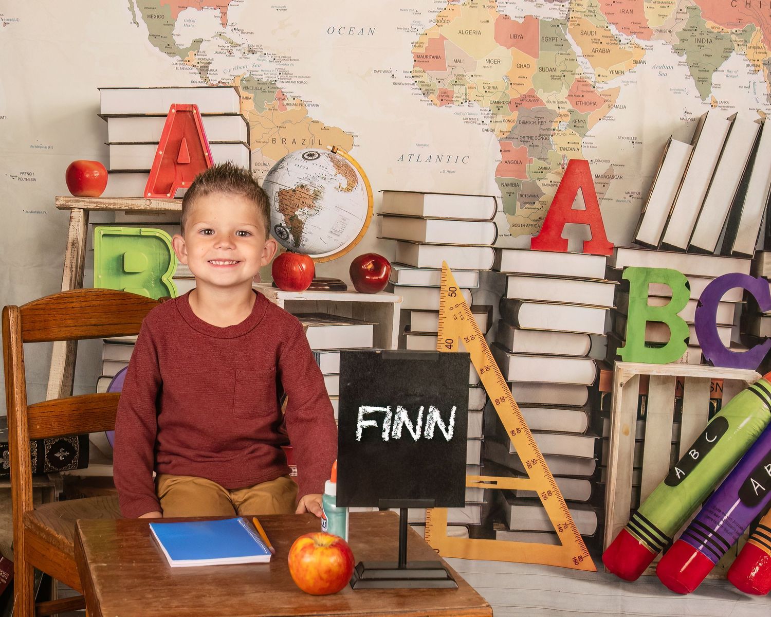 Back to school scene with colorful alphabet letters, stacked books, apples and chalkboard displaying name Finn.
