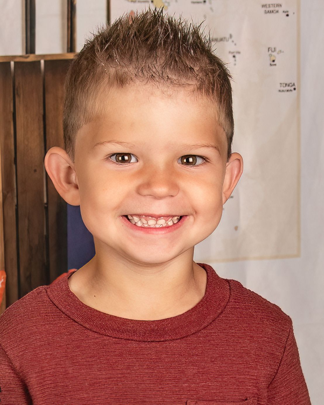 Young child wearing a burgundy t-shirt smiles brightly at the camera.