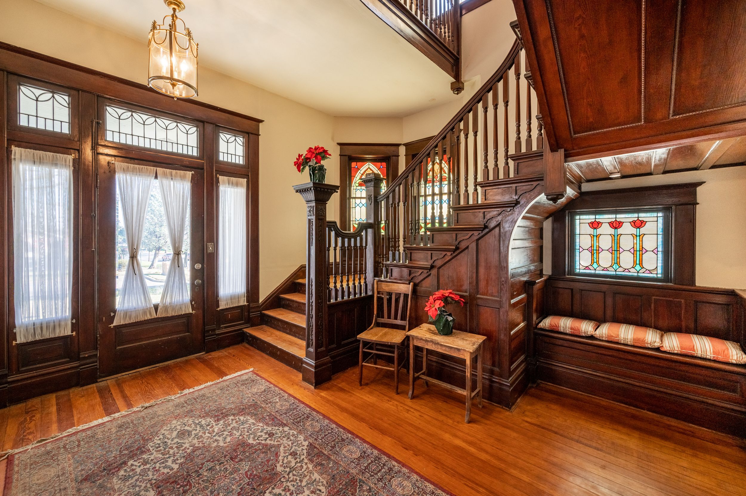 Grand wooden entryway with ornate staircase, built-in bench, and hardwood details in a traditional home.