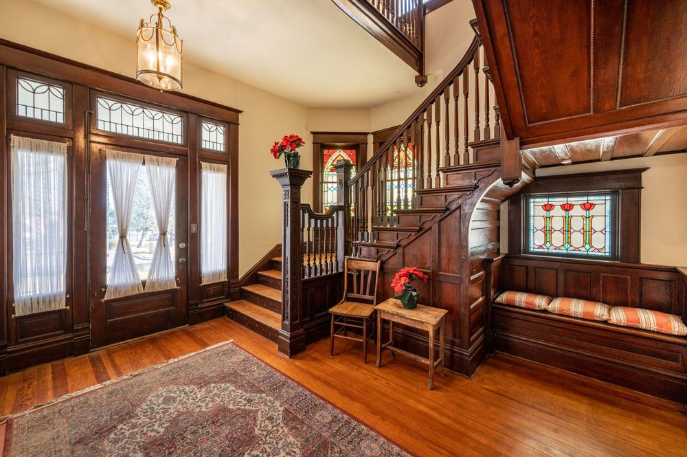 Grand wooden entryway with ornate staircase, built-in bench, and hardwood details in a traditional home.