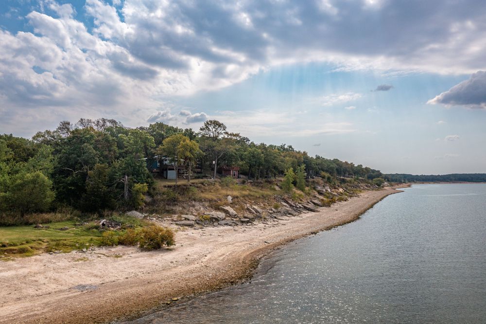 Scenic shoreline with sandy beach and wooded bluffs along a serene lake under cloudy skies.