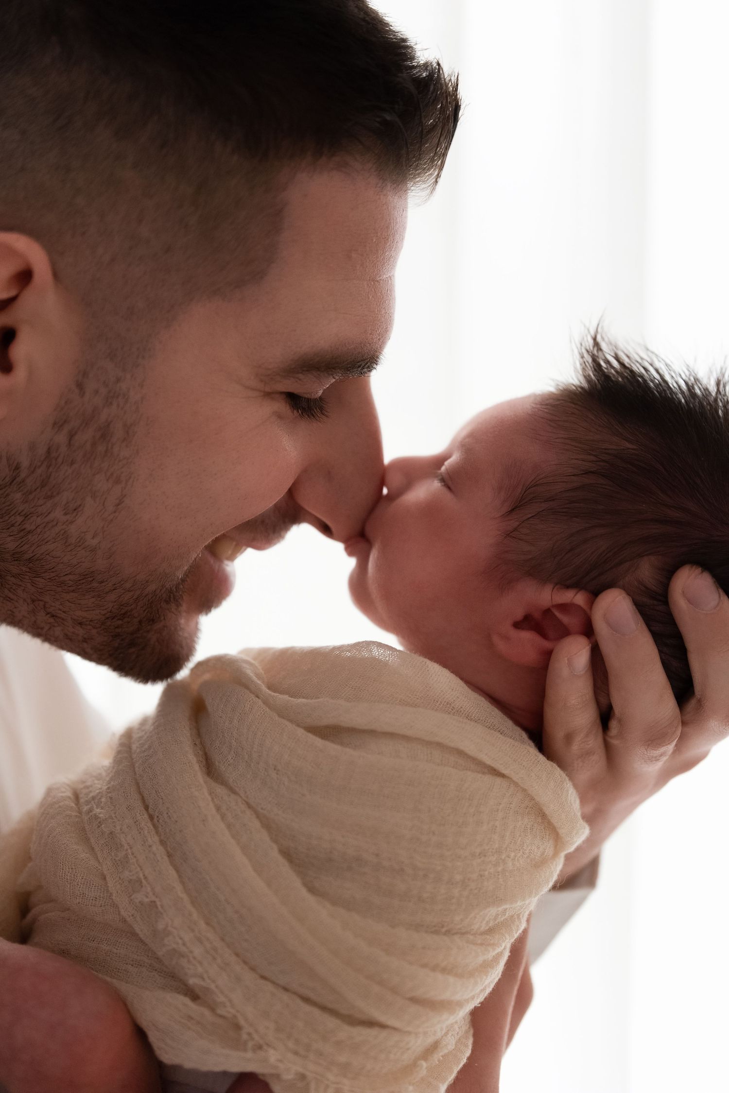 Loving father touching noses with his swaddled newborn baby in a tender moment.