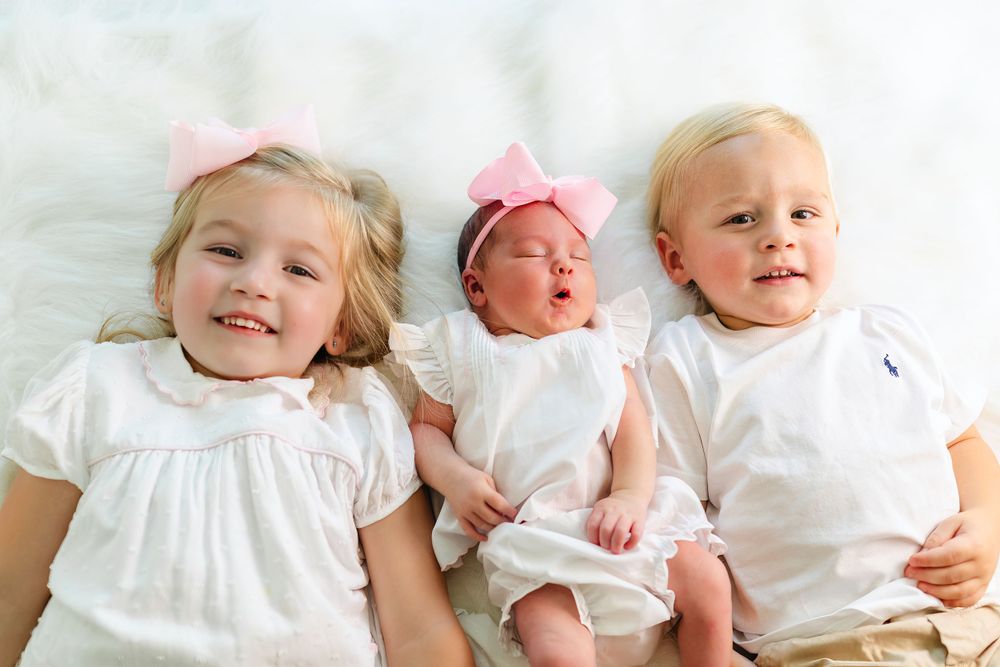 Multiple views of baby in white dress with pink bow on light background.