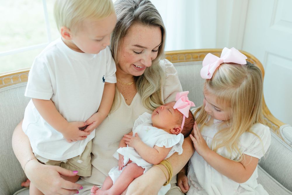 Family gathering on white couch to welcome new baby in matching white outfits.