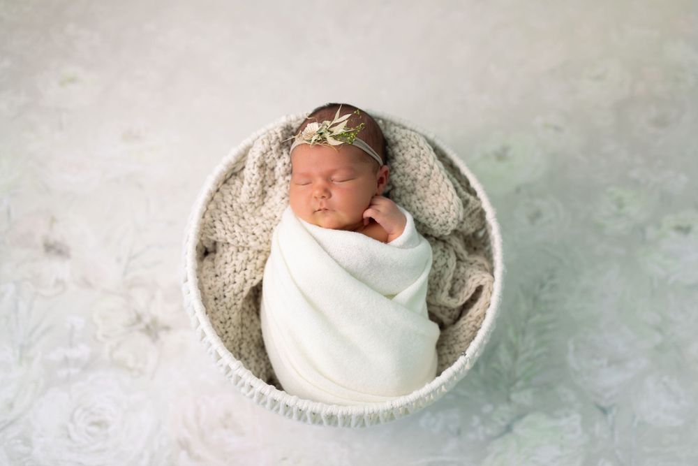 Newborn baby sleeping peacefully in white wrap on textured grey backdrop.
