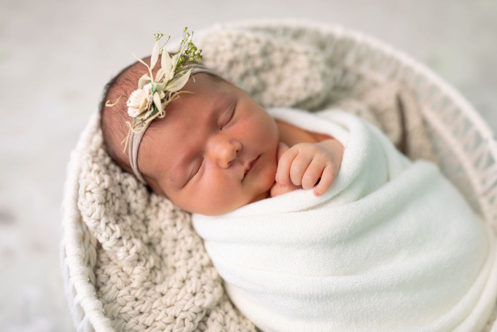 Sleeping newborn baby swaddled in white blankets on soft textured background.