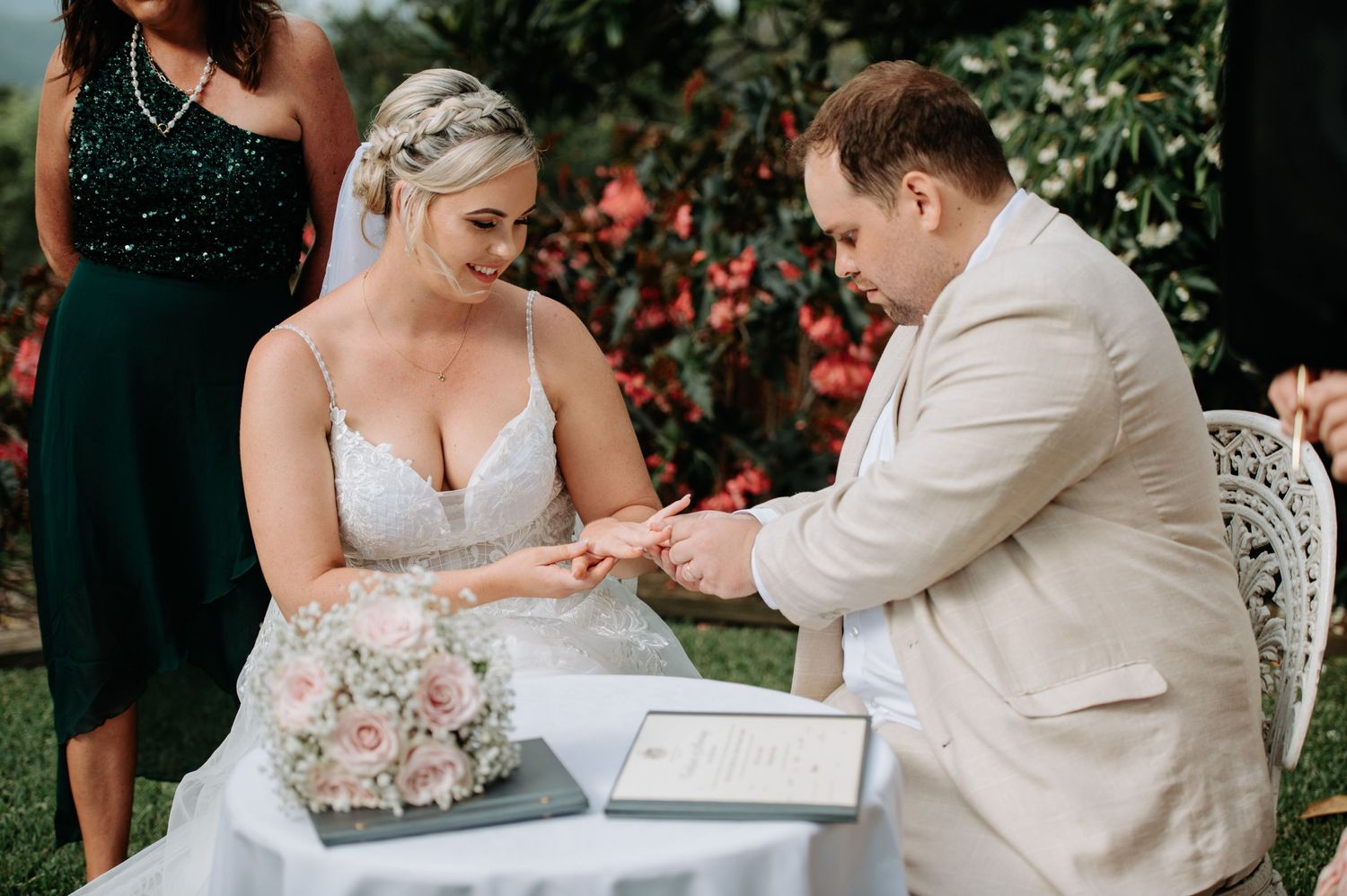 Wedding ceremony moment during ring exchange with floral bouquet on signing table.