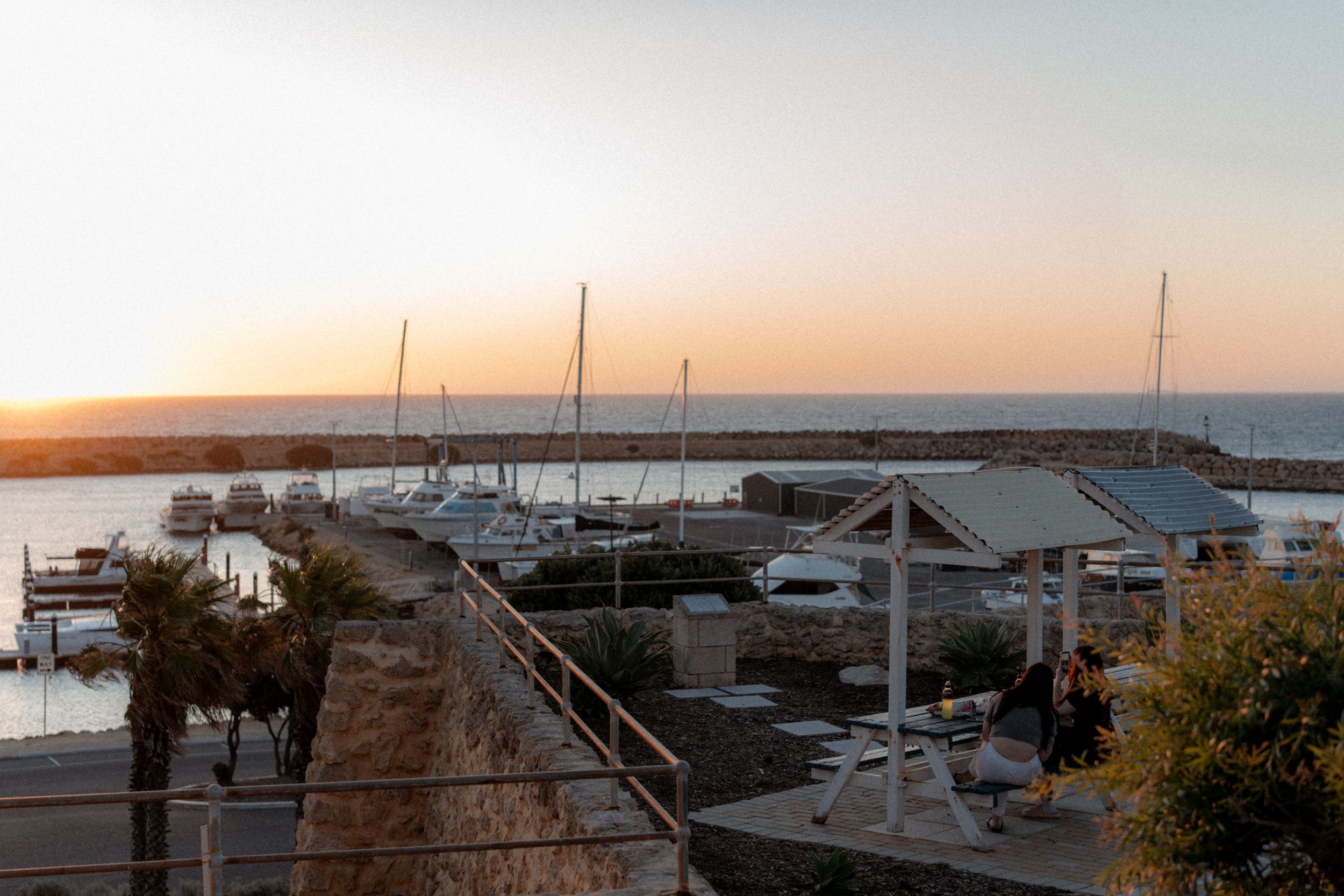 Sunset view over a marina with sailboats and buildings along the waterfront during golden hour.