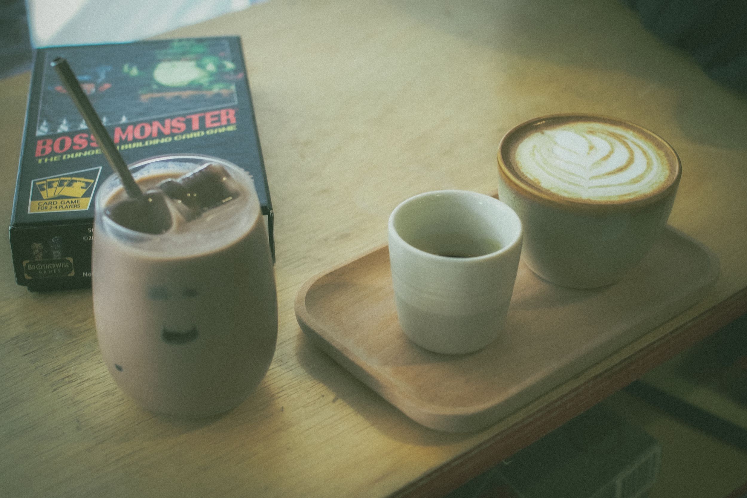 Coffee setup with a latte art drink, empty cup, and brewing equipment on a wooden serving board.