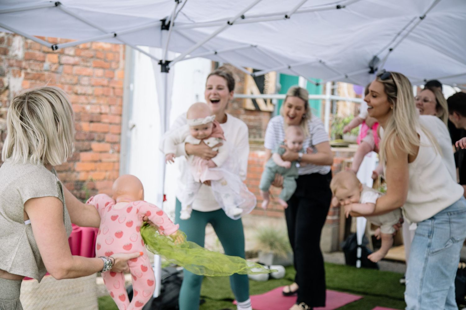 Group activity under white tent with baby toys and outdoor setting.