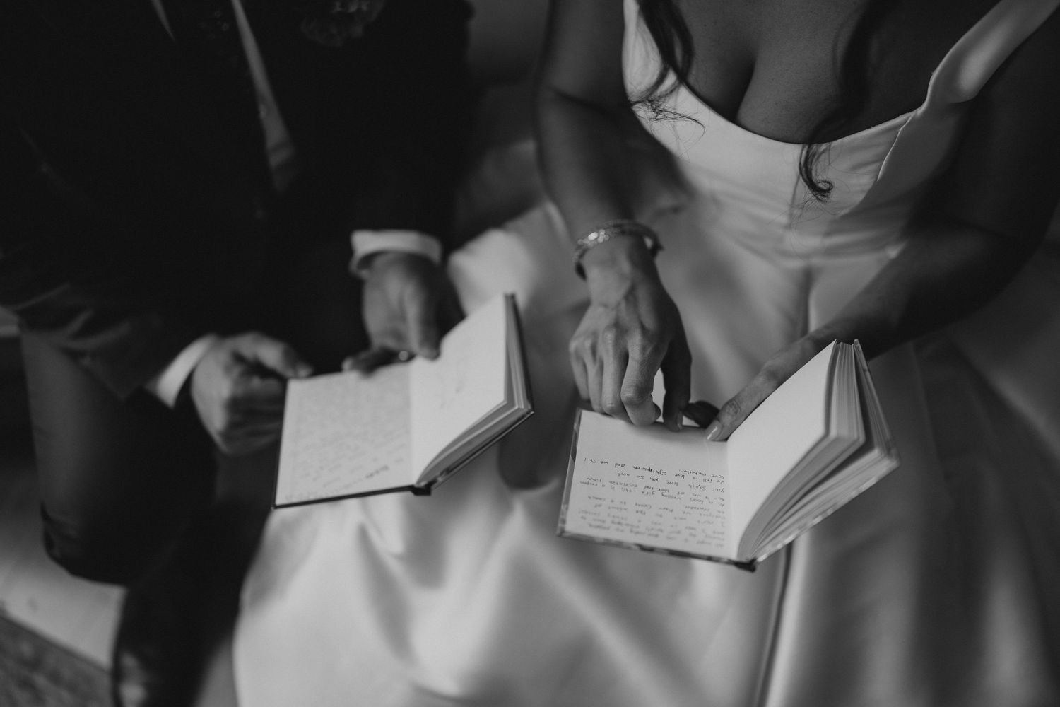 Black and white photograph of hands holding an open book in wedding attire.