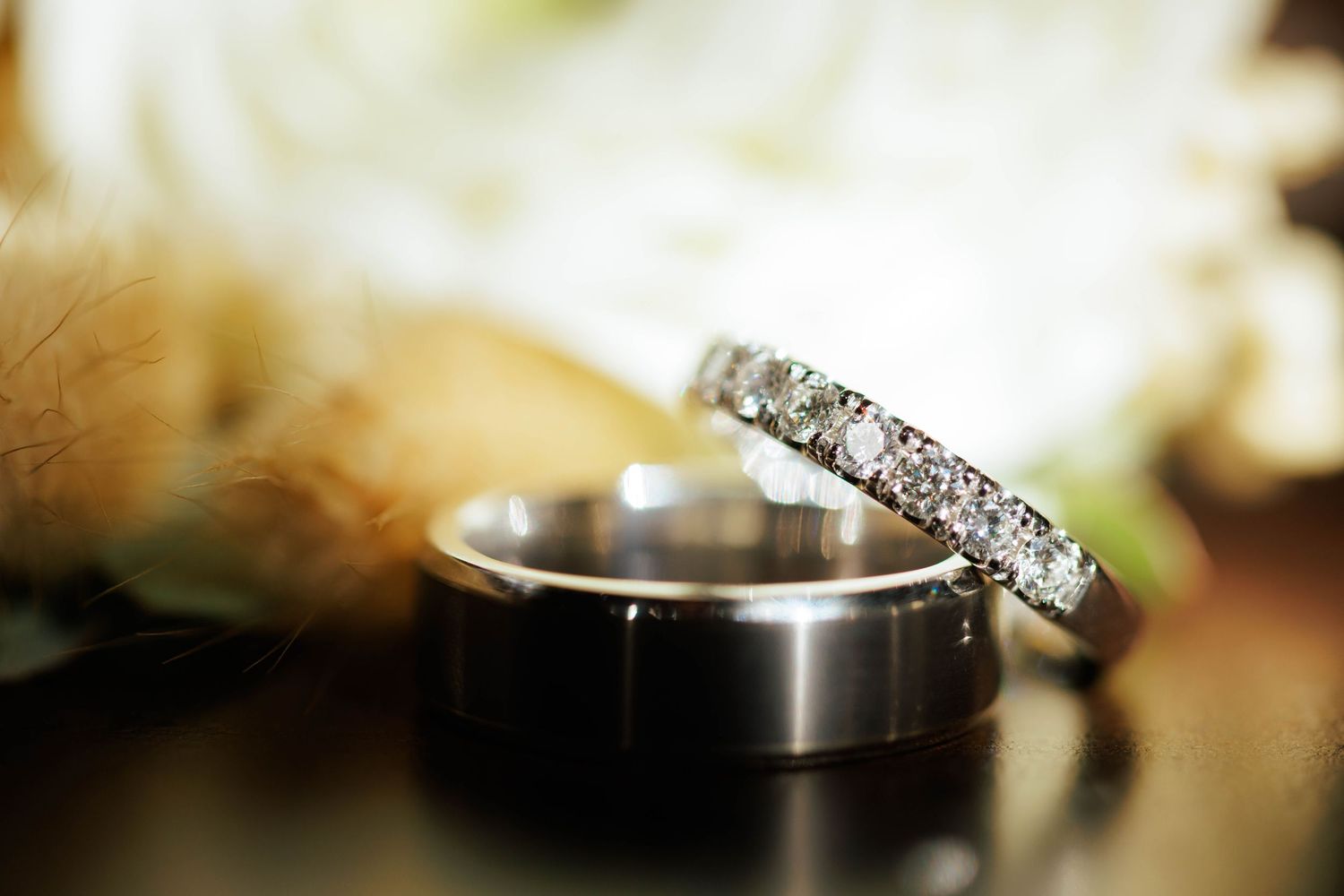 A close-up of two wedding rings, one diamond eternity band and one plain band, with soft floral bokeh.