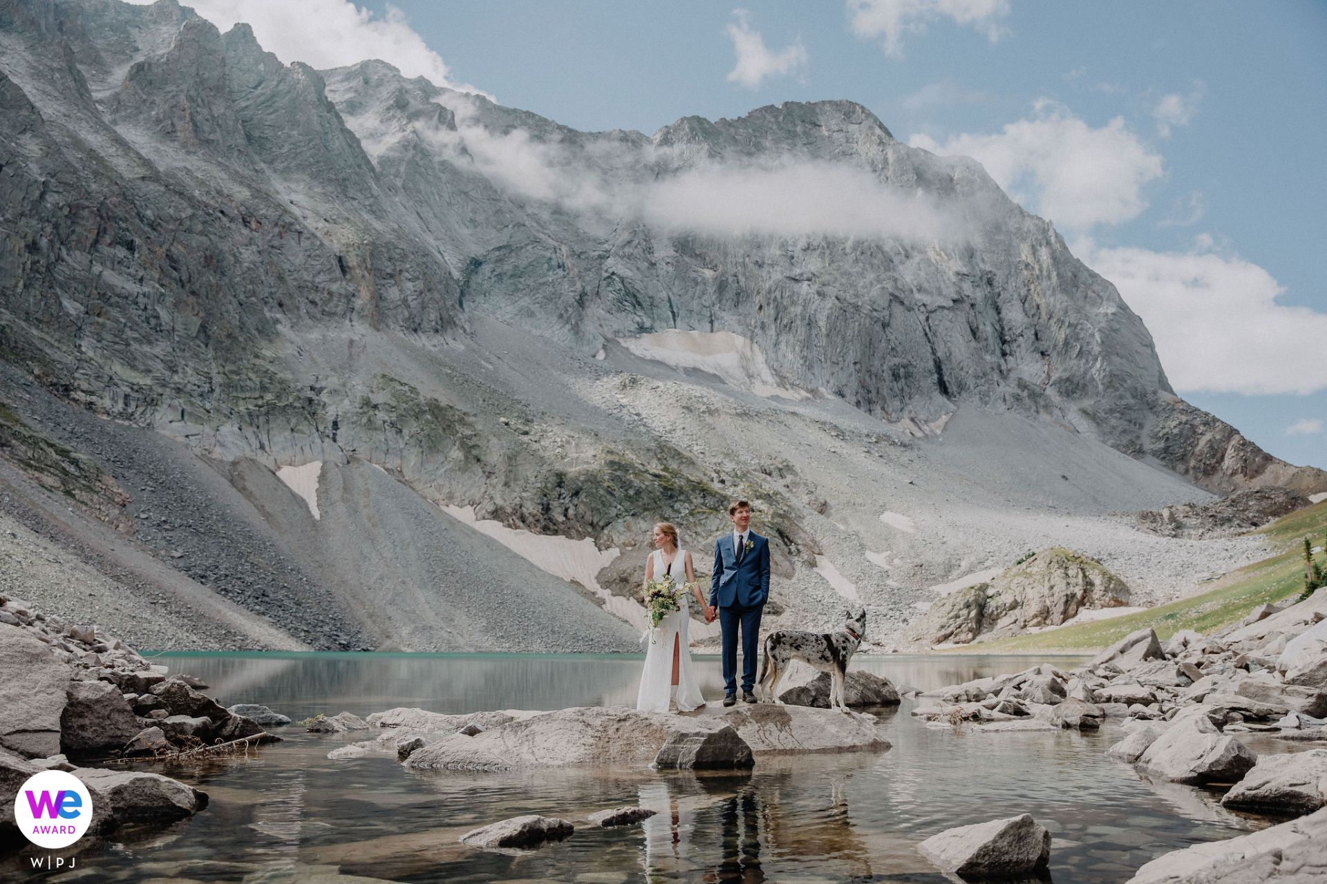A stunning wedding portrait captured by a mountain lake surrounded by rugged alpine peaks.