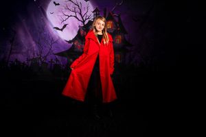 Figure in bright red coat poses dramatically against eerie purple Halloween night scene with full moon.