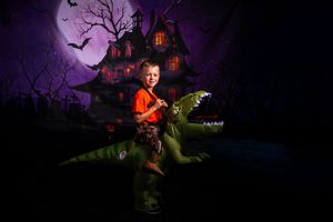 Halloween night scene with haunted mansion, flying bats, and dark trees against an eerie purple sky.