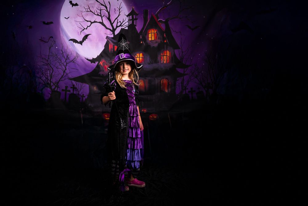 A spooky haunted house silhouetted against a purple night sky with bats flying and glowing windows.
