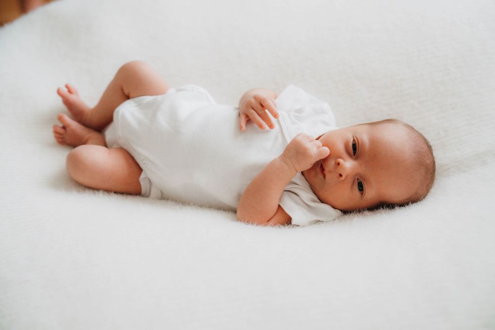 A newborn baby lies on soft white bedding in a series of connected photos showing different angles and poses.