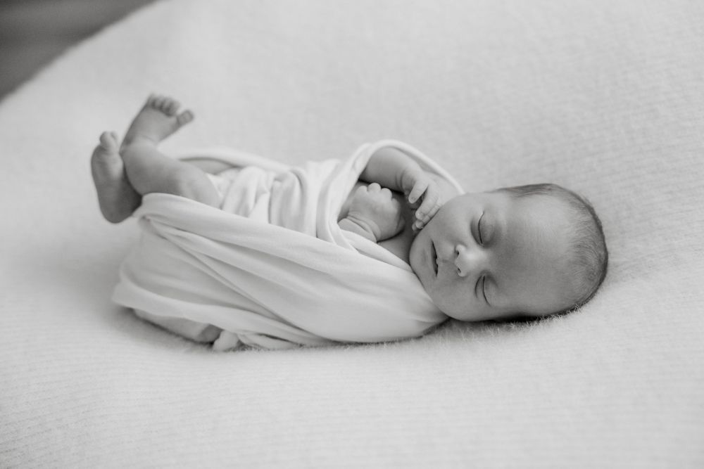 Peaceful newborn baby sleeping on soft white blanket in minimalist monochrome photography.