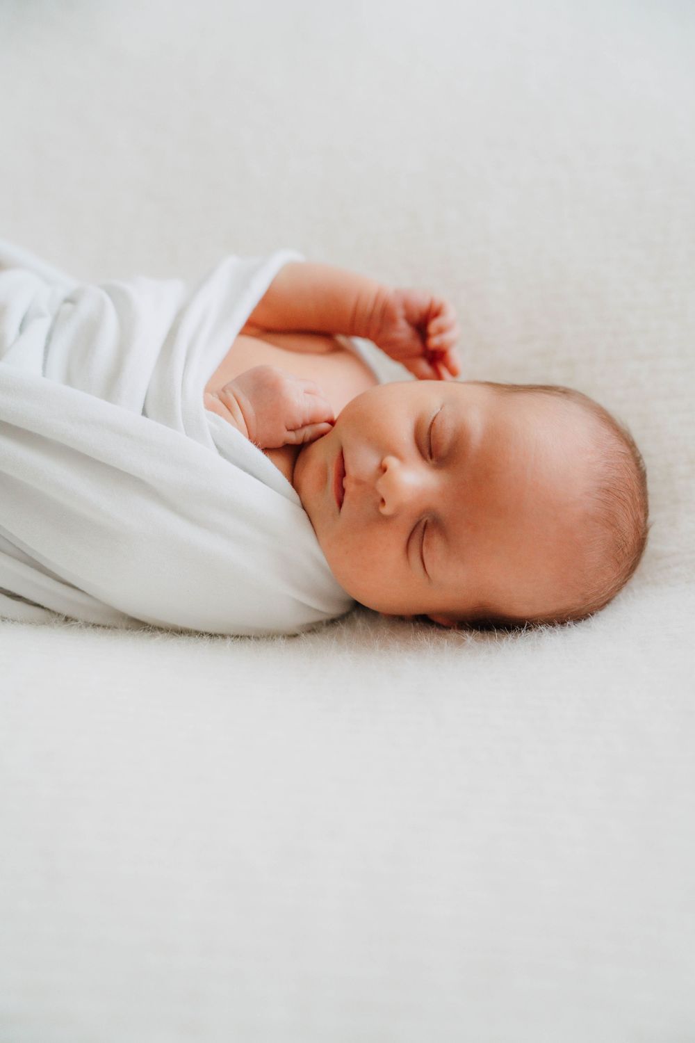 Peaceful sleeping baby wrapped in soft white blankets against light background.
