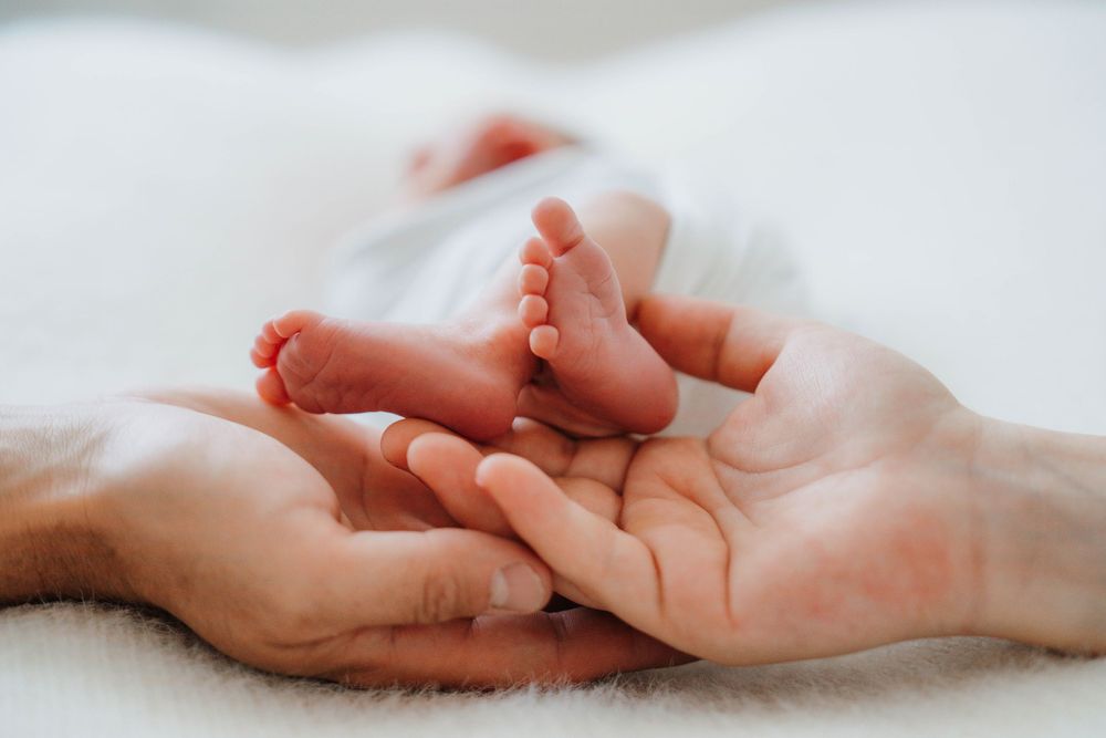 Tender sequence showing adult hands holding delicate newborn feet on white sheets.