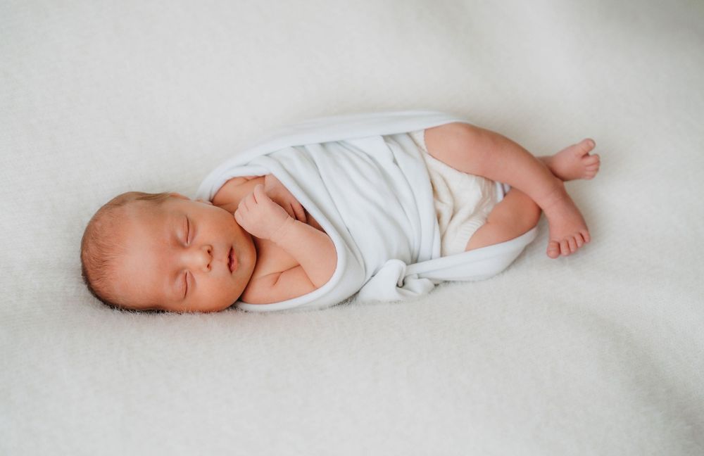 A newborn baby in white clothing lying on soft white bedding shown in multiple poses from different angles.