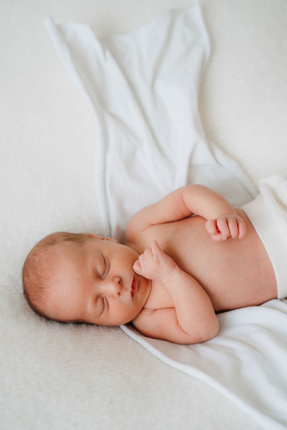 Newborn baby sleeping peacefully on white sheets in a series of artistic close-up photos.