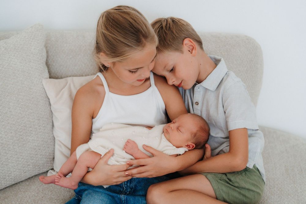 Family bonding moment on a light gray couch while feeding a newborn baby.