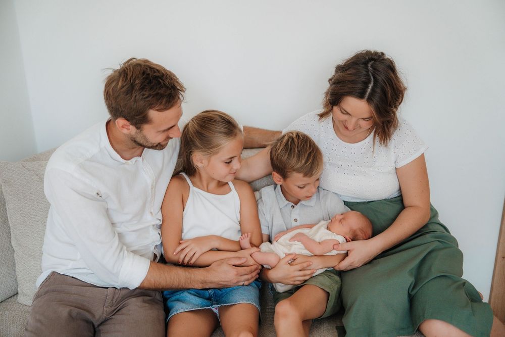 Family gathered together on couch sharing intimate moment with newborn.