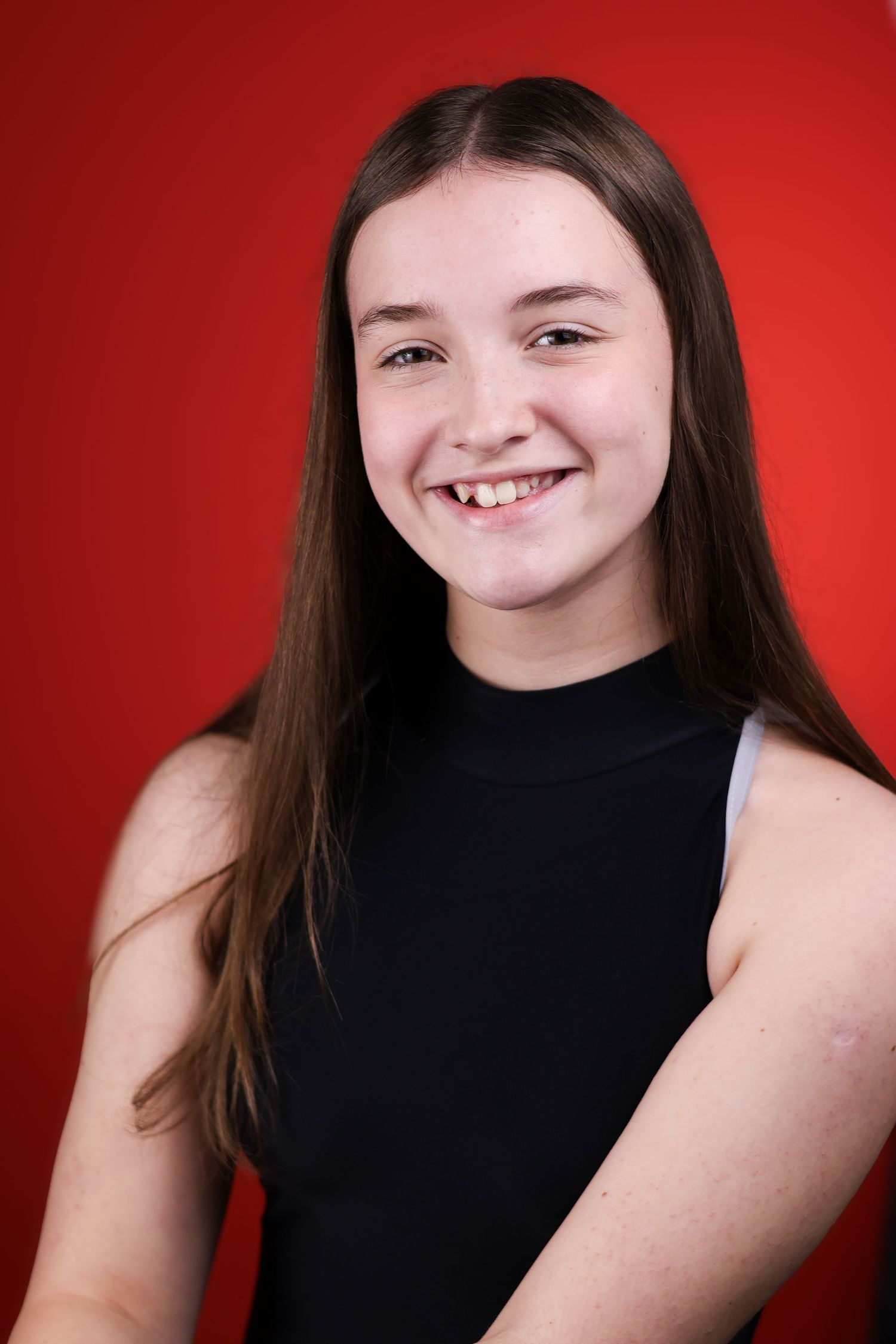 Portrait with red backdrop showing genuine smile and sleeveless black top.