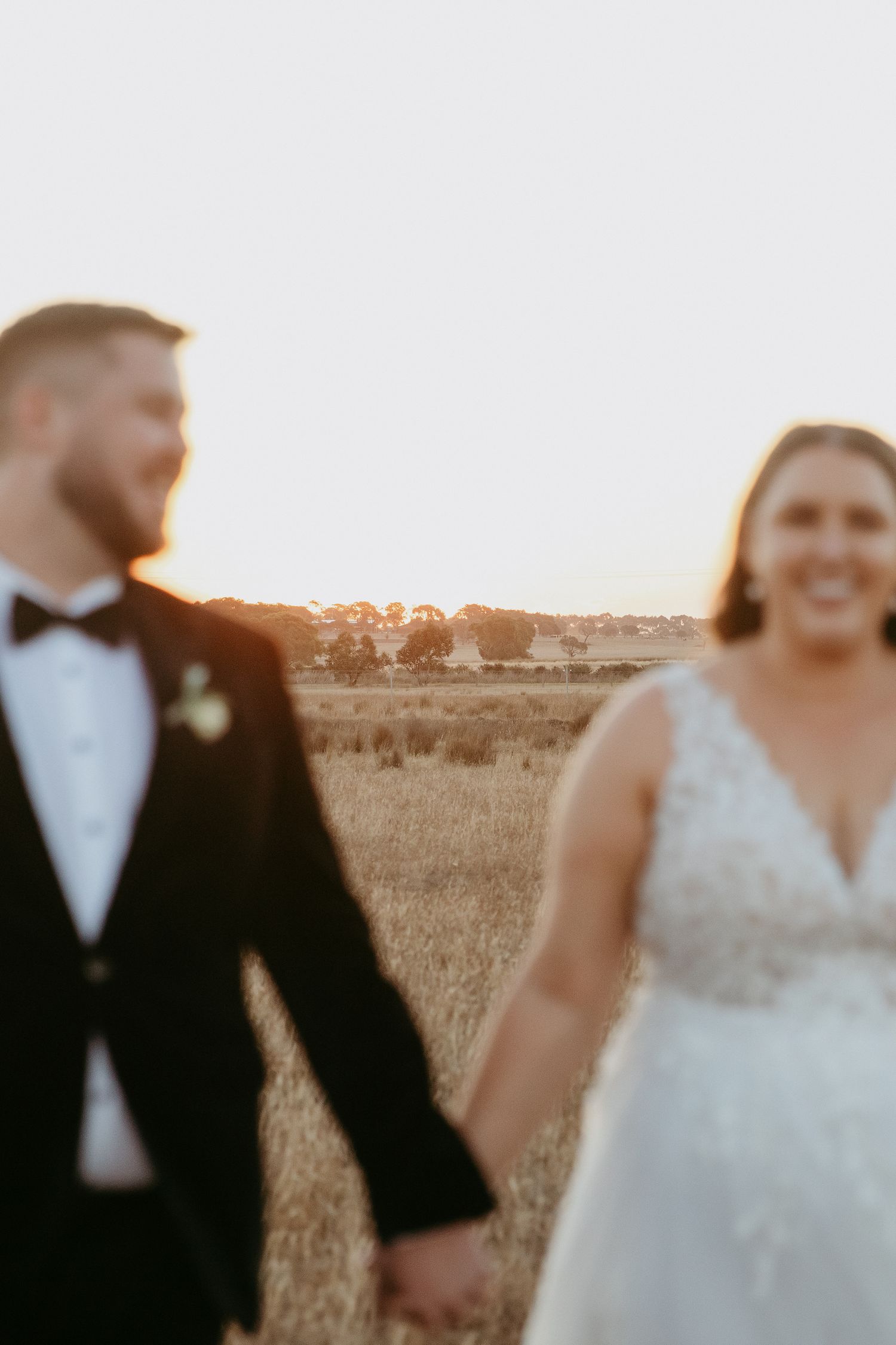 Couple out of focus with the farmland behind them at sunset on the One Day Estate Winery, Curlewis, Victoria