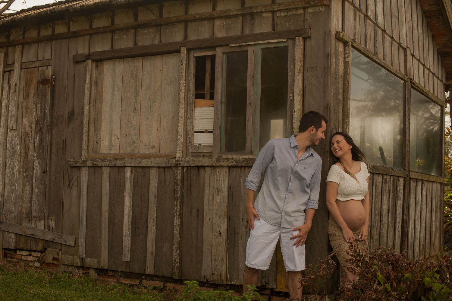 A couple poses against weathered wooden walls of a rustic cabin.